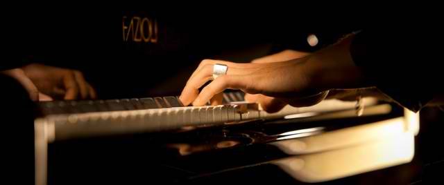 Les mains d’un pianiste sur le clavier d’un piano Fazioli, dans une lumière chaleureuse